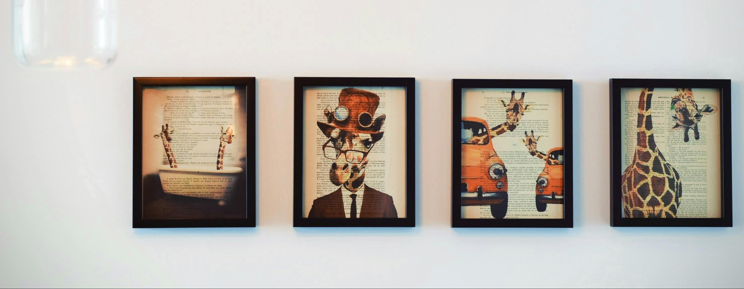 Four framed artworks of animals on a white wall with two hanging lights.